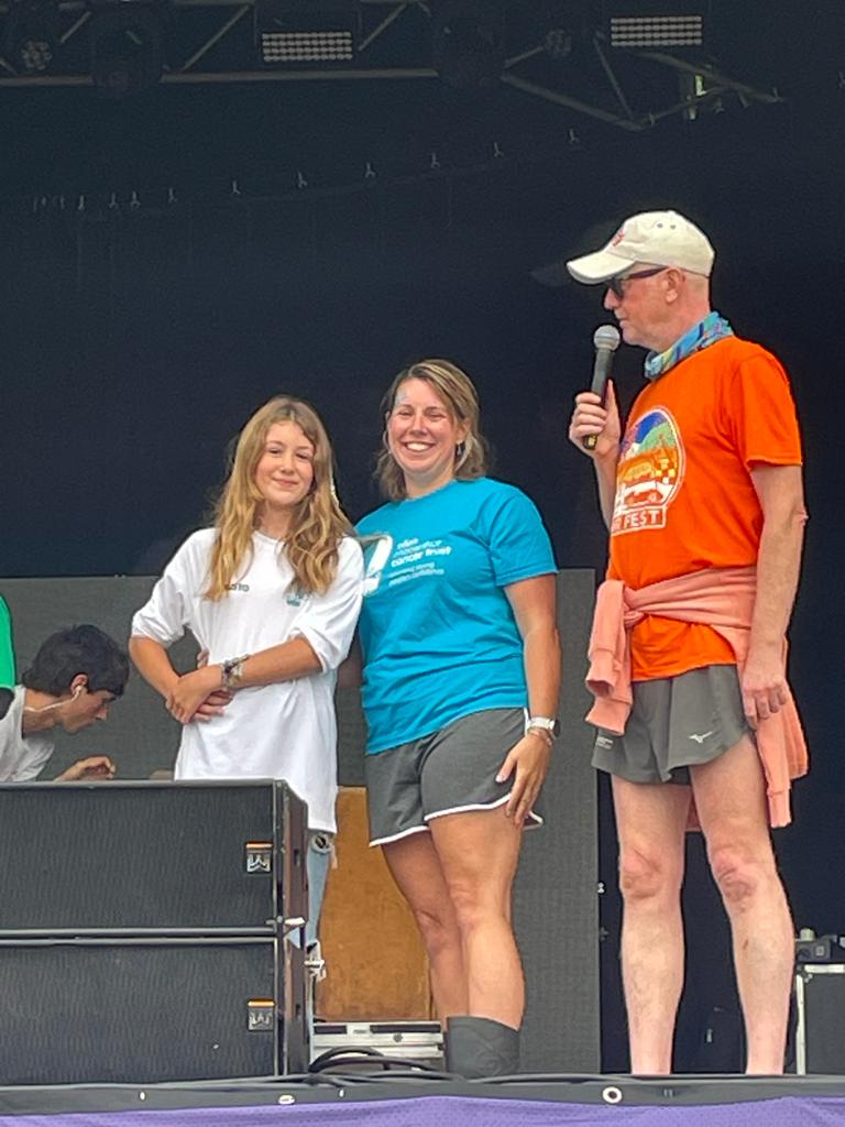Bella smiling on stage at CarFest standing beside Jade from the Trust and festival founder Chris Evans