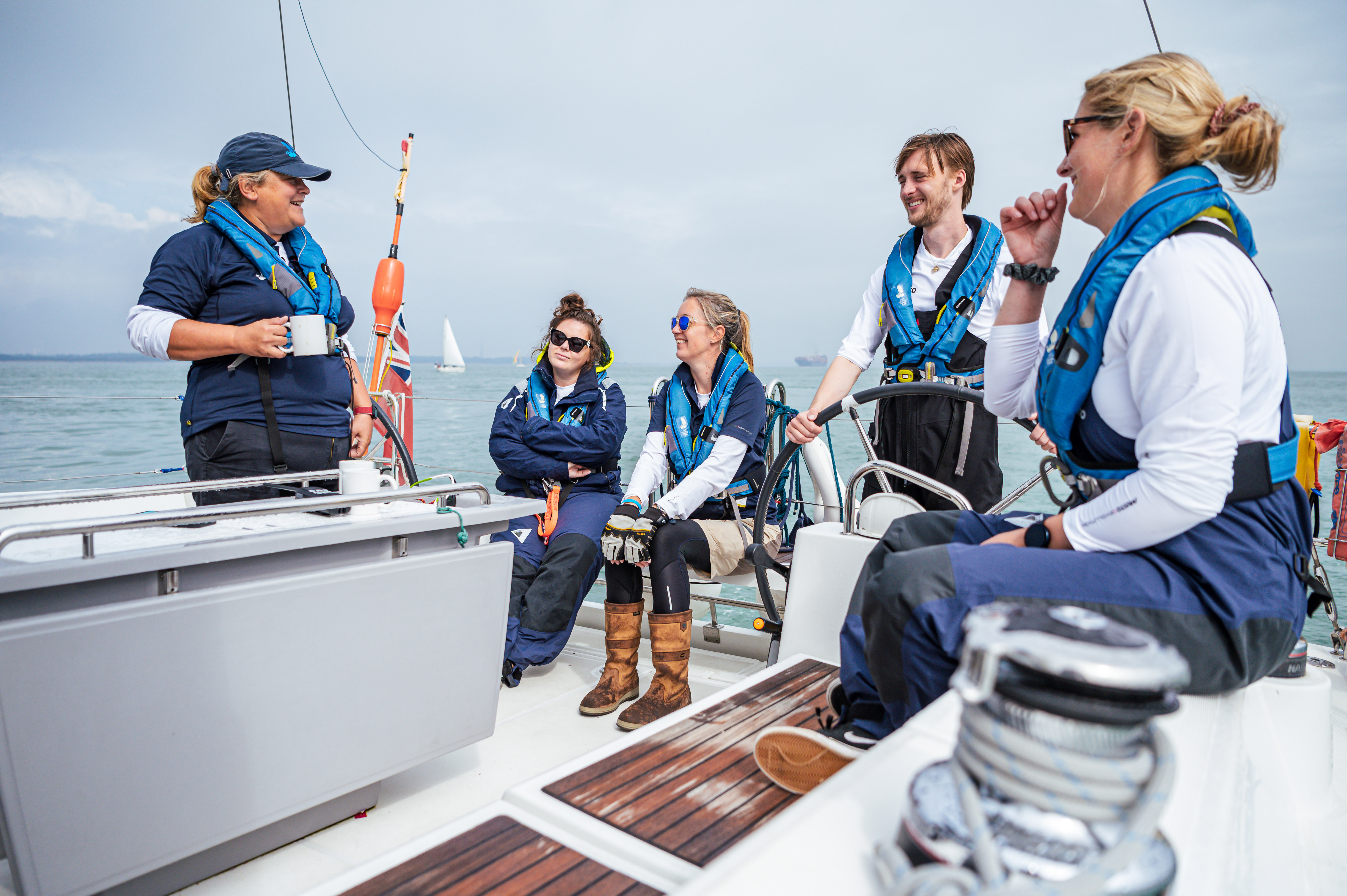 A crew of young people, aged over 18, and Trust crew are sailing and smiling up the back of a yacht