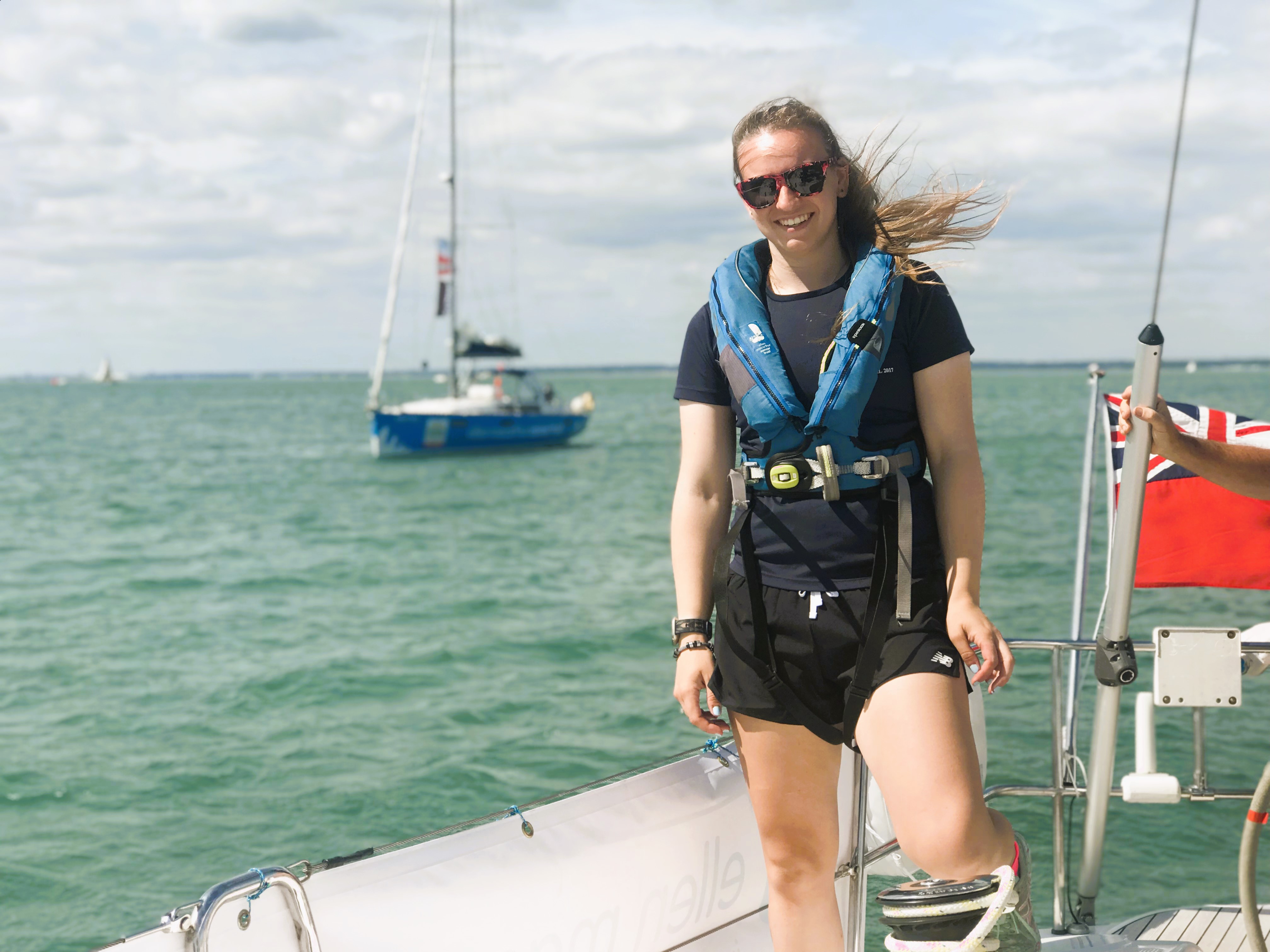 Lucie standing on deck during a sailing adventure with the Trust on a sunny day, smiling at the camera with sunglasses on