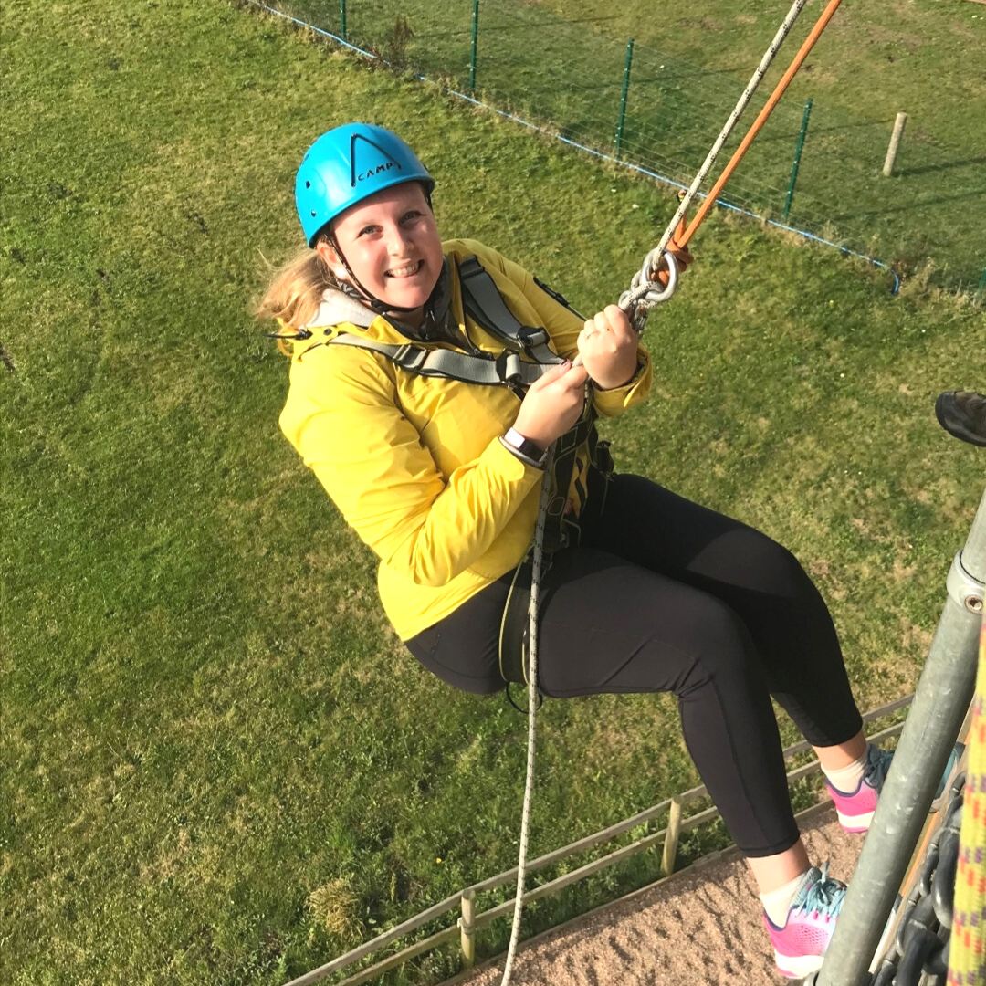 Fran wearing a bright yellow jacket and blue helmet as she abseils