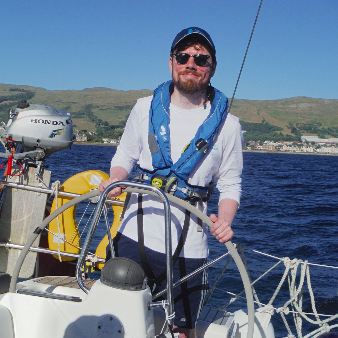 Ewan at the helm with the stunning scottish hills behind him 