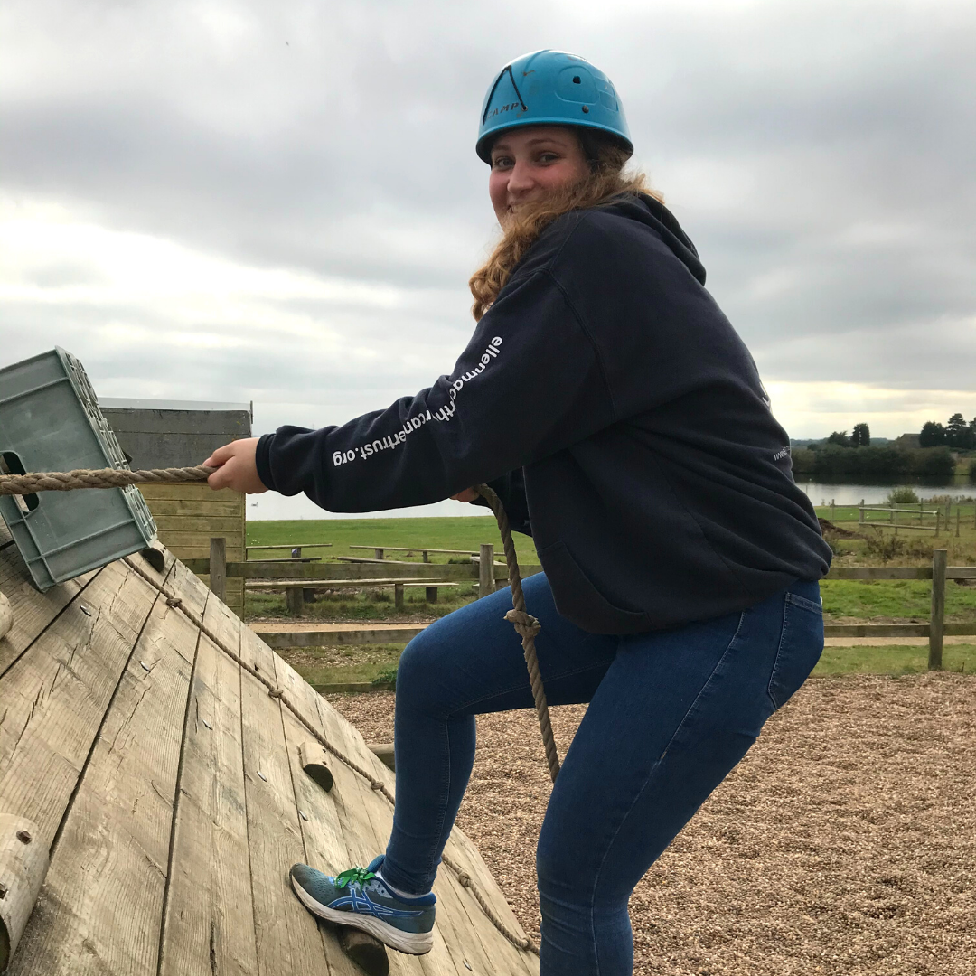 Holly wearing a blue helmet and Trust hoodie on a climbing wall during volunteer training