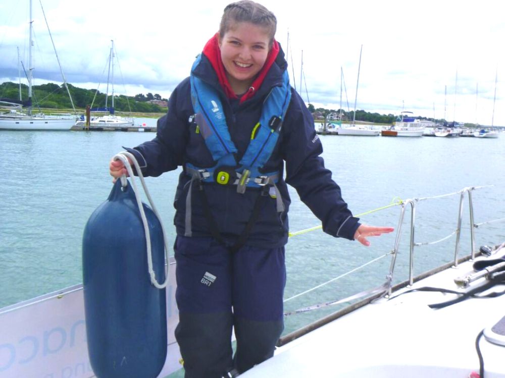Libby Berridge holding a fender and smiling on a Trust boat with the blue sea in the background