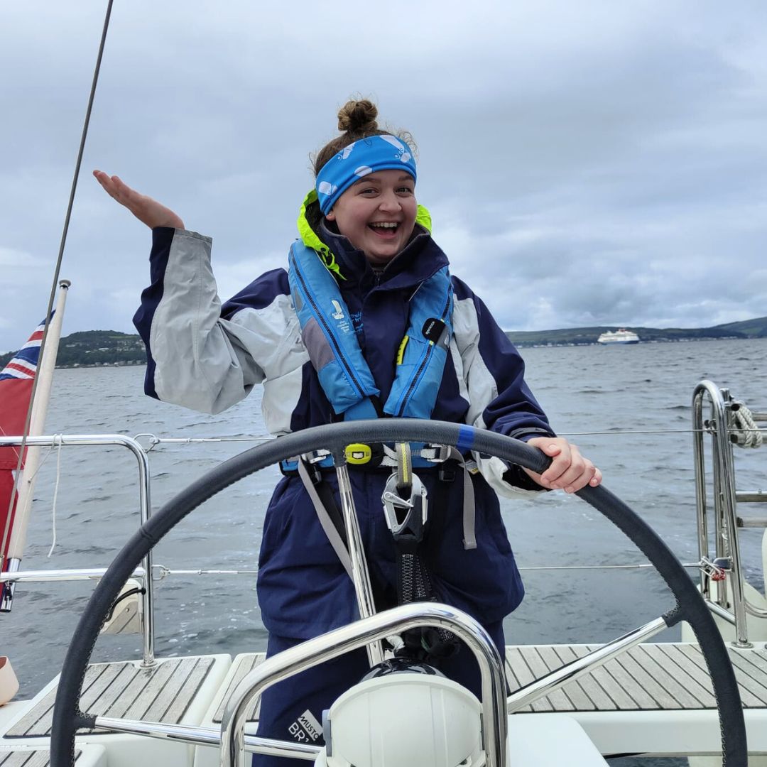 Lucy with a big smile on her face while helming in Largs on a grey day