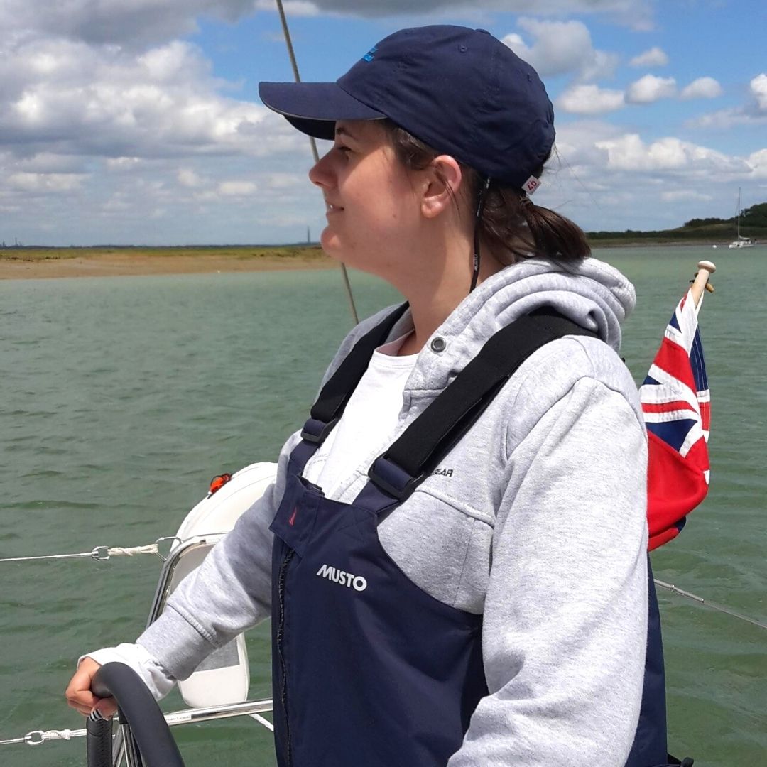 Becca Austin at the helm looking ahead to the sun with the sea in the background